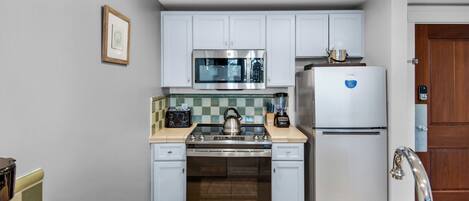 A compact kitchen with white cabinets, a stainless steel refrigerator, a microwave, a stove, and a sink.