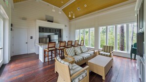 A spacious living area with a kitchen, large windows, and a wooden ceiling. - Steps From Baytowne Wharf With Pool & Private Beach Access (Miramar Beach)