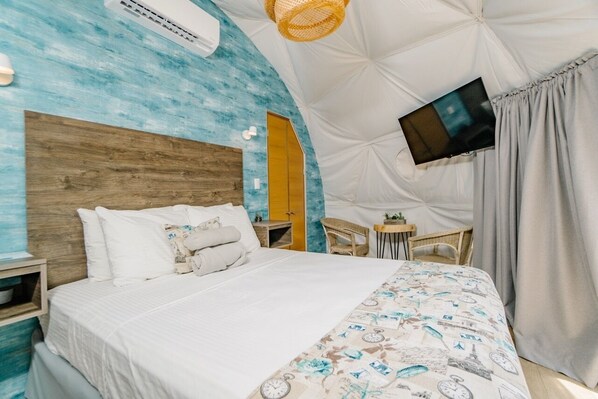 A bedroom with a bed, a TV mounted on the wall, a small table, and a chair. - Tortuga Verde Glamping (Sardinal)
