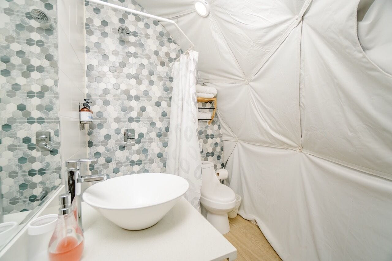 Une salle de bain moderne avec un lavabo blanc, une douche dont le carrelage présente un motif hexagonal et des toilettes.