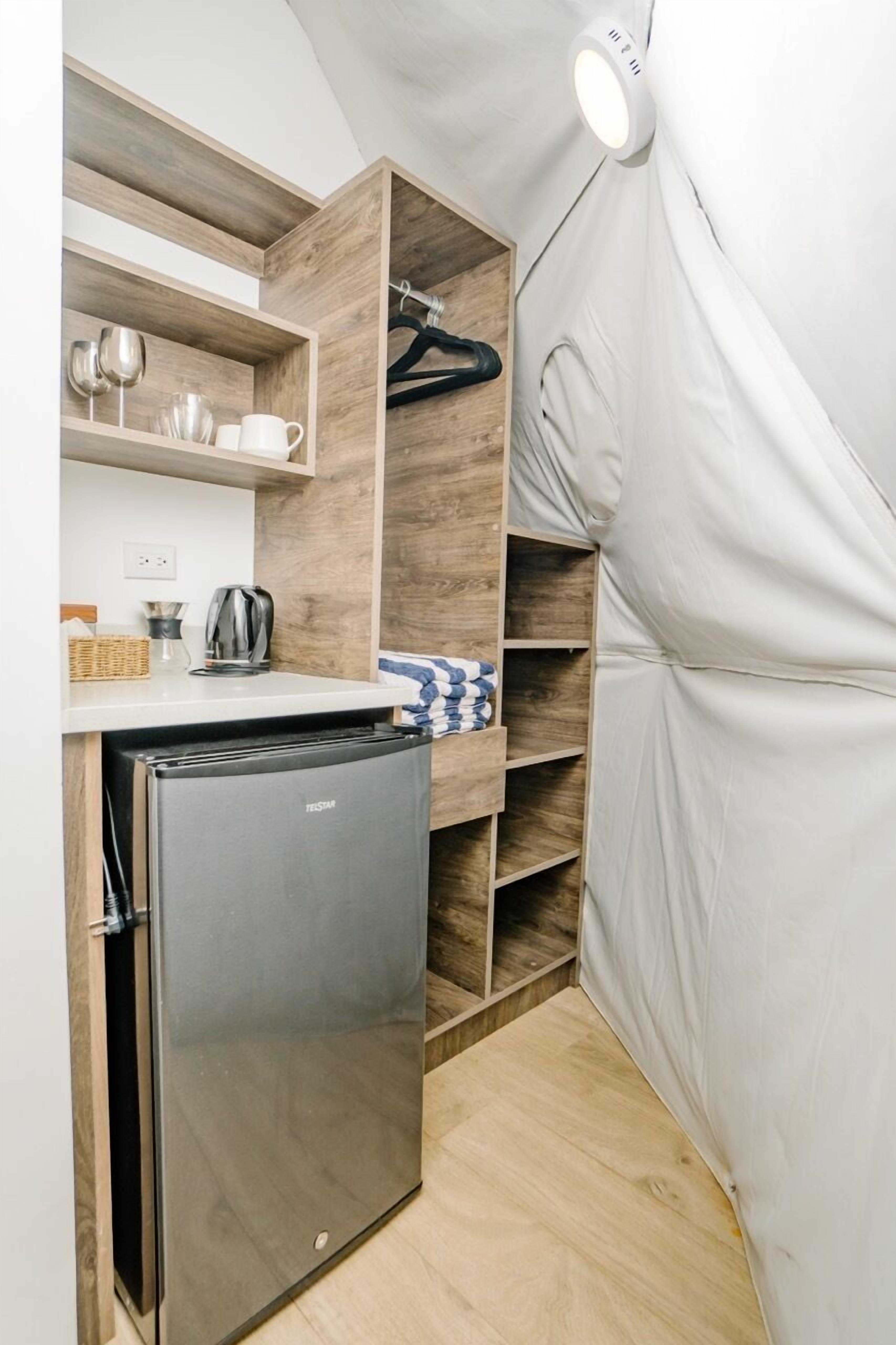 A compact kitchenette with a built-in refrigerator, wooden shelves, and a hanging rack.