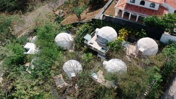 Zona residencial con varias estructuras en forma de cúpula en medio de la vegetación, rodeada por una casa con techo de tejas rojas.