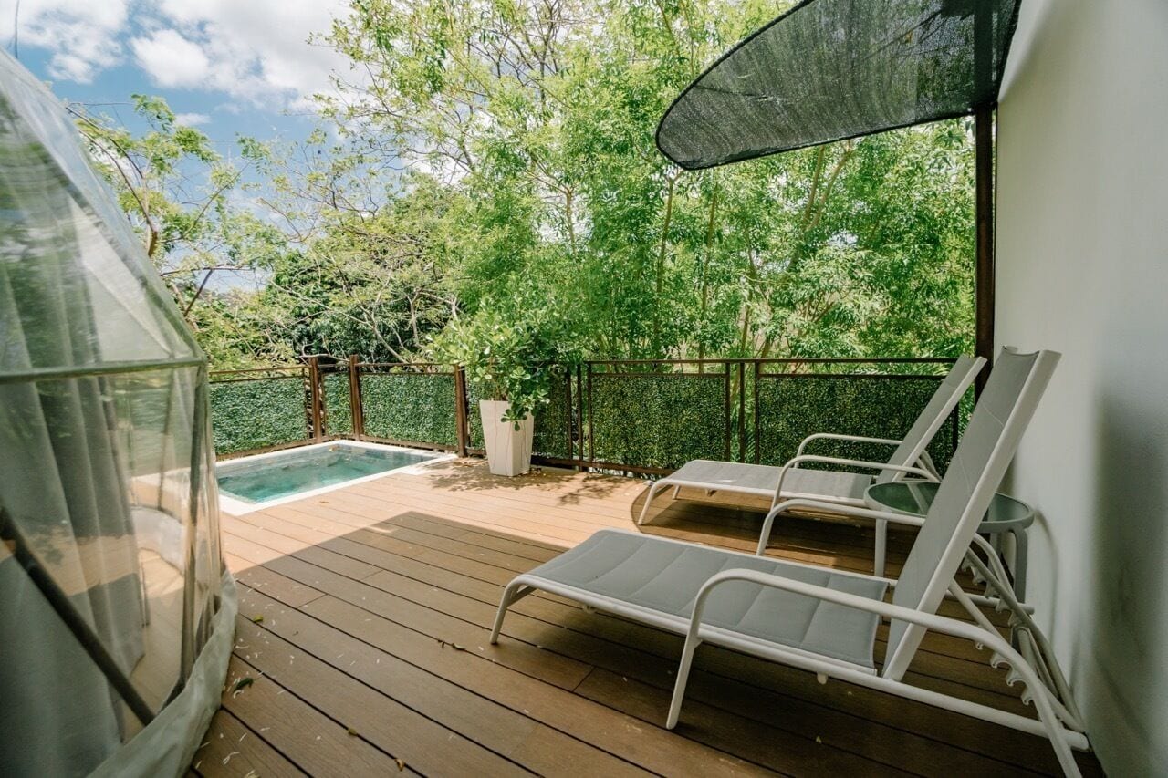 A wooden deck with two white lounge chairs, a small pool, and a covered area with a mesh screen.