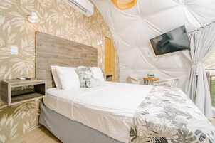 A bedroom with a bed, a bedside table, a TV mounted on the wall, and a window with curtains.