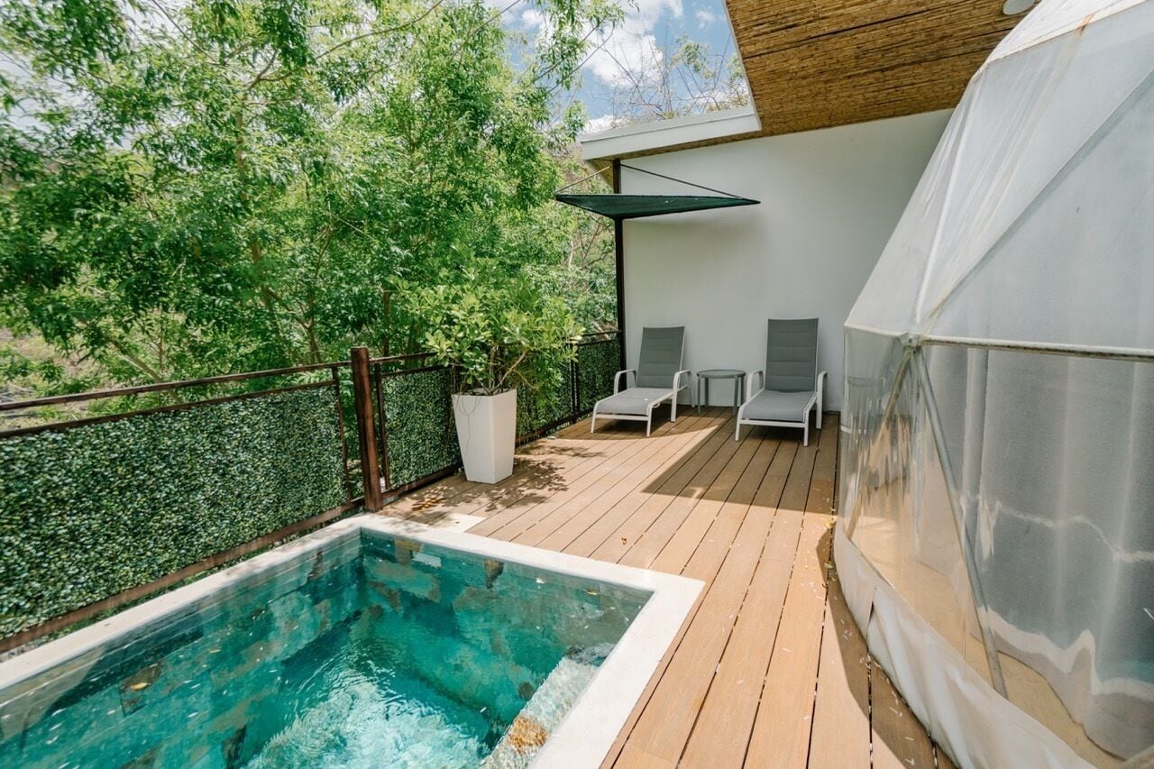 A wooden deck with a swimming pool, lounge chairs, and a covered area.