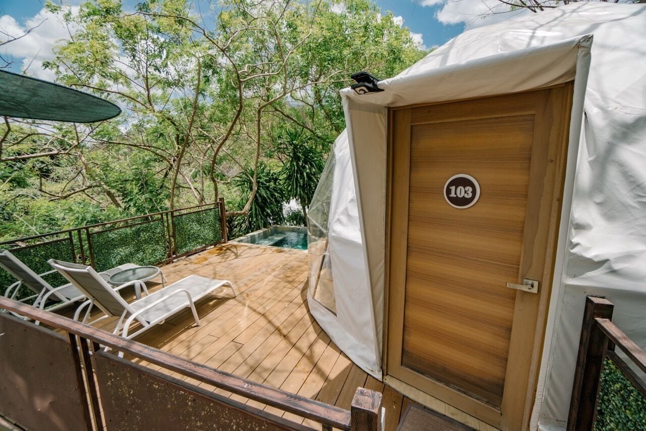 Terraza de madera con sillones de descanso, una piscina y una carpa con el número 103.