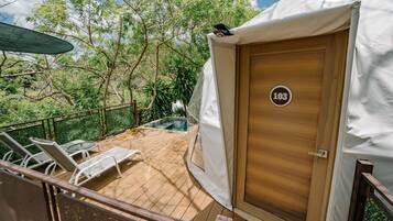 Terraza de madera con sillones de descanso, una piscina y una carpa con el número 103.