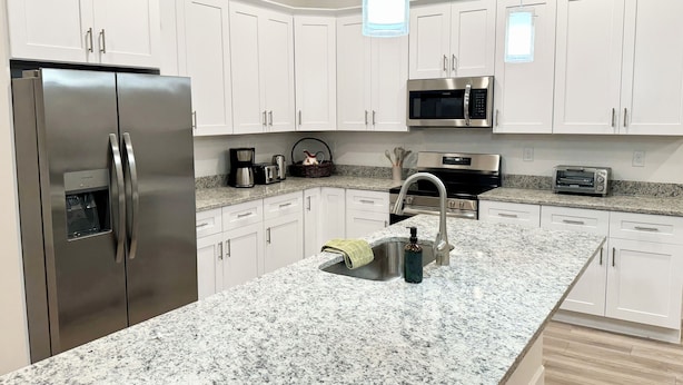 Una cocina moderna con armarios blancos, electrodomésticos de acero inoxidable, encimeras de granito e iluminación colgante.