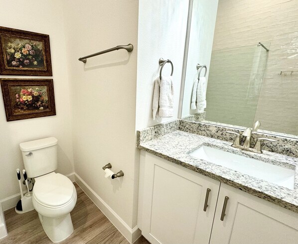 A bathroom with a toilet, sink, and mirror. There are two framed floral paintings on the wall.