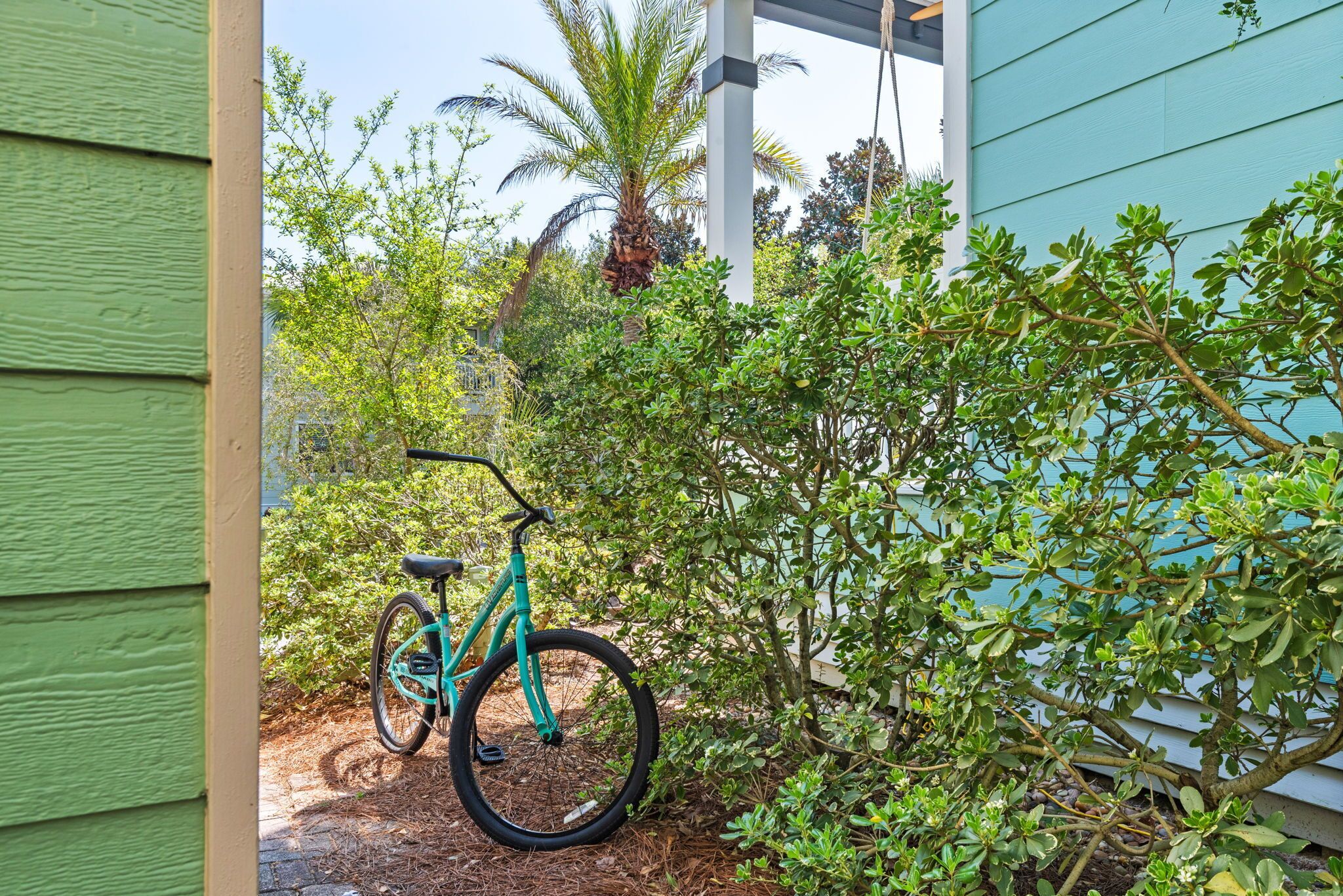 A turquoise bicycle parked near a green house with a porch.