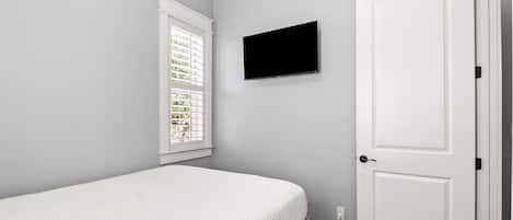 A bedroom with a bed, a window with blinds, a television on the wall, and a door.