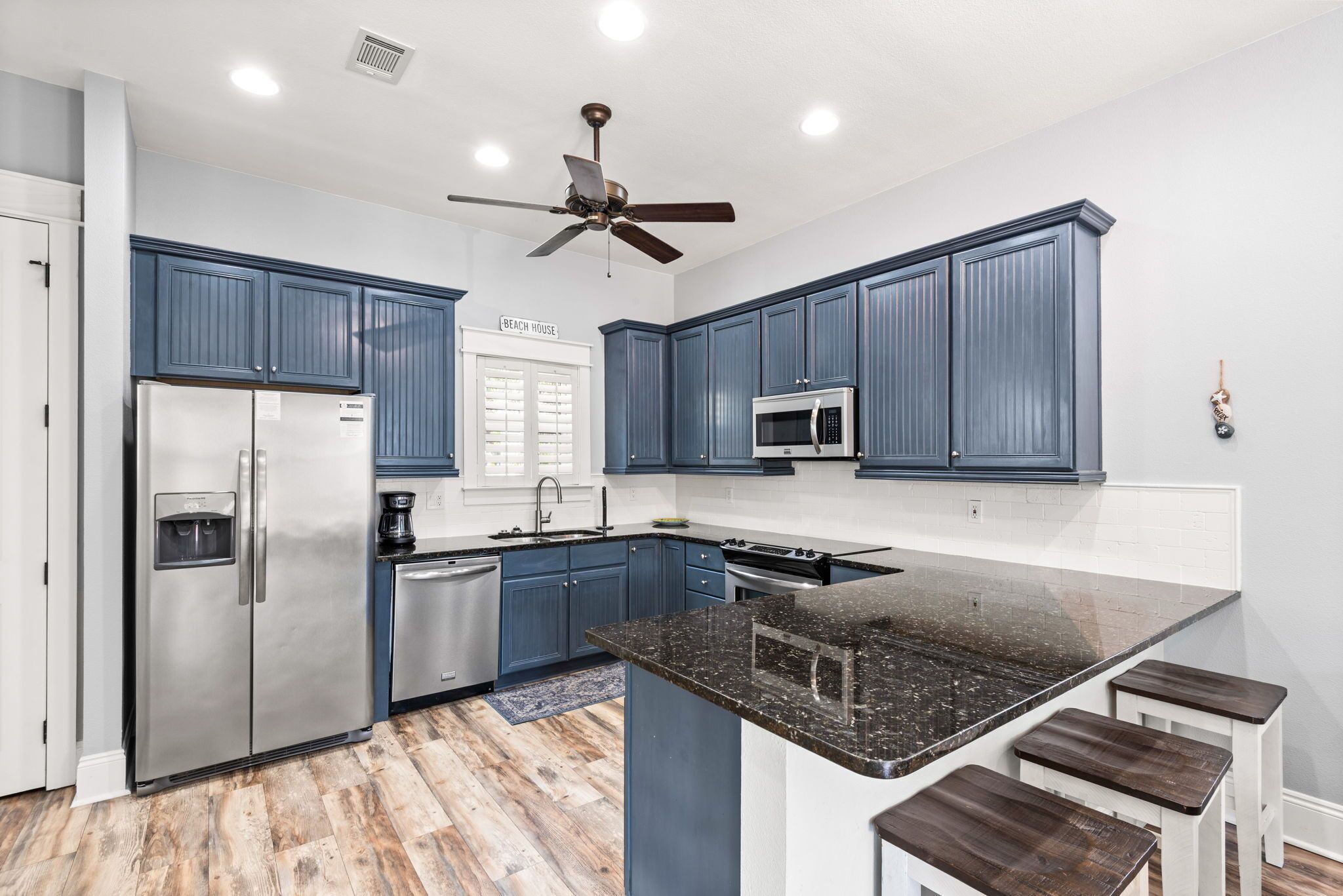 A modern kitchen with blue cabinets, stainless steel appliances, a central island, and a ceiling fan.