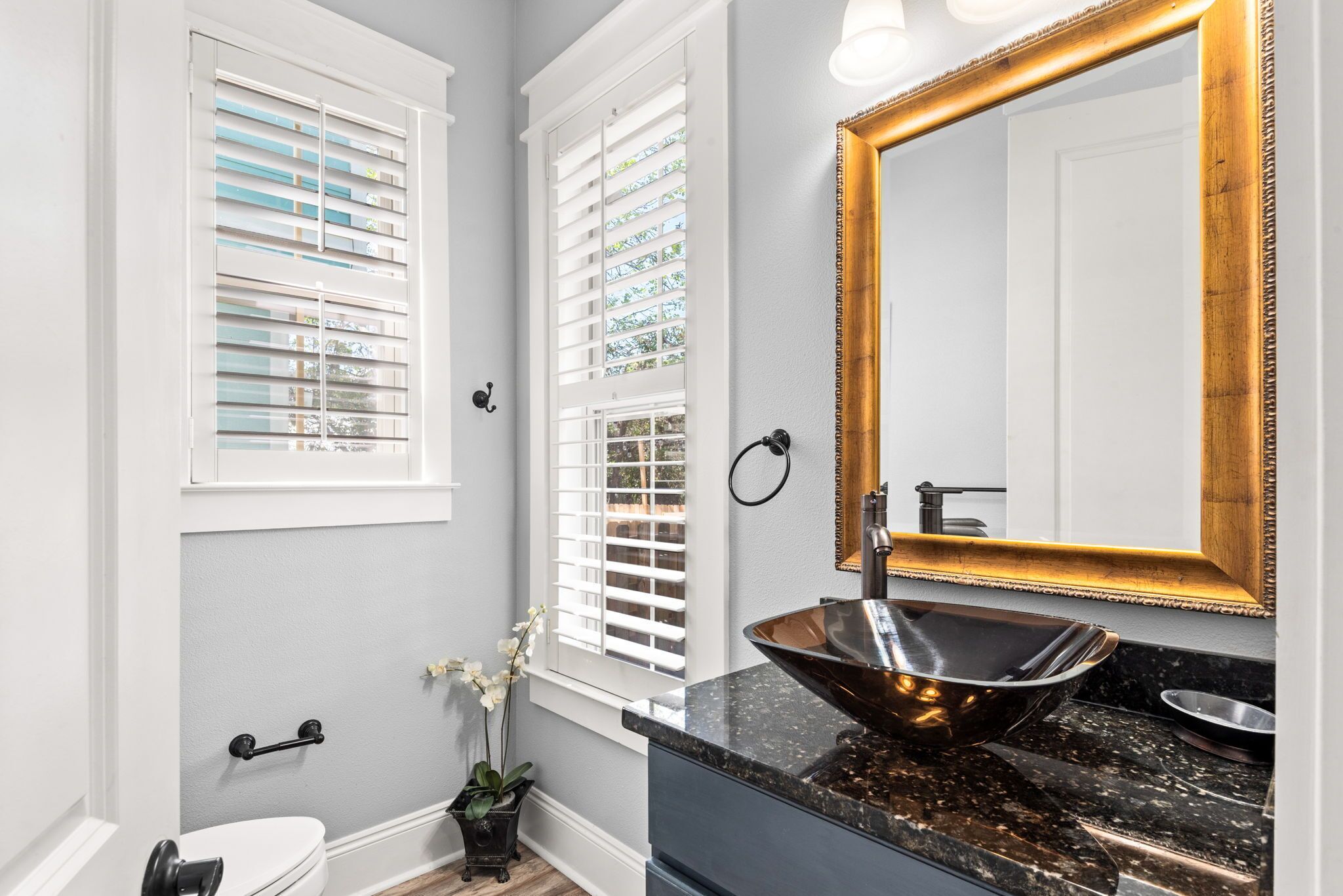 A bathroom with a vessel sink, a large mirror, and a window with blinds.