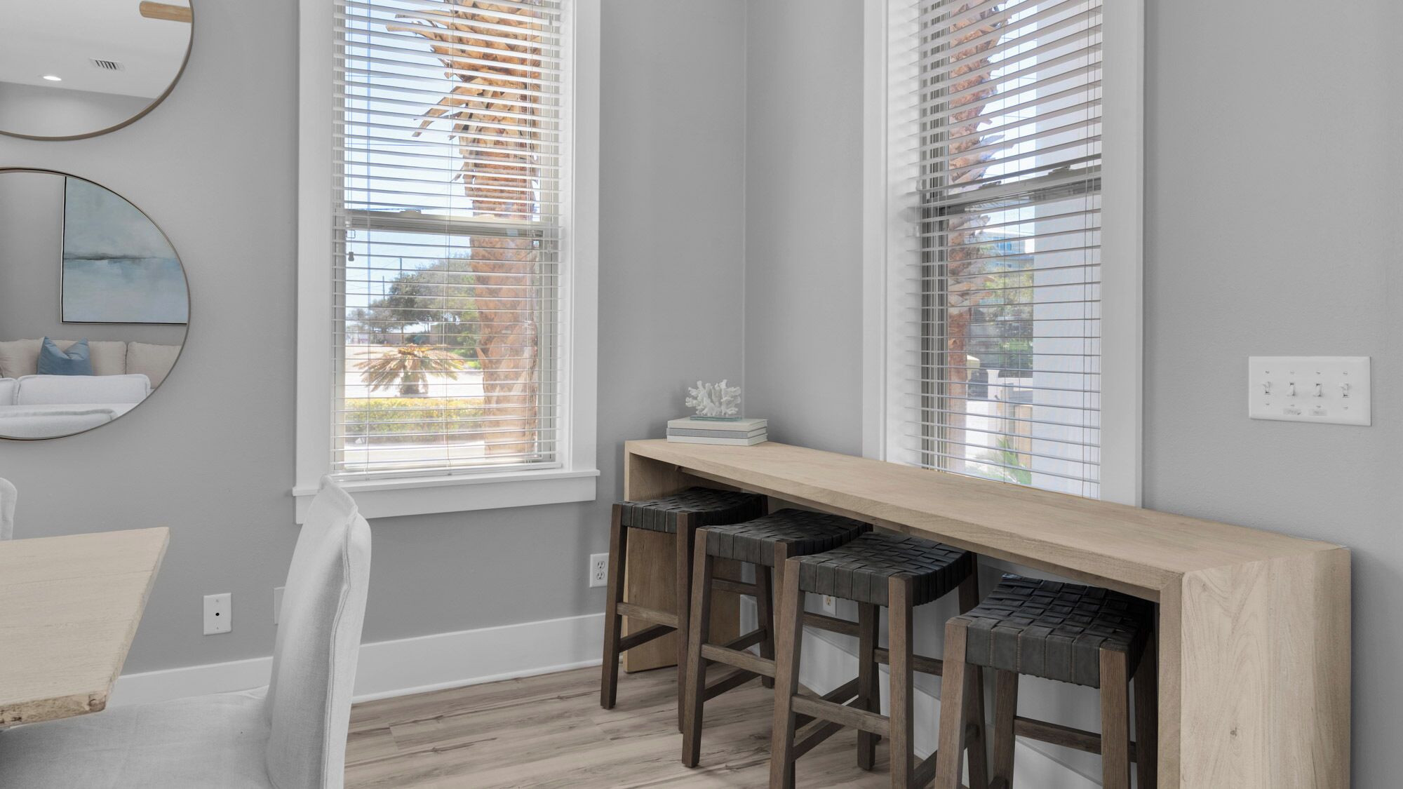 A modern kitchen with a wooden countertop, bar stools, and a large window with blinds.
