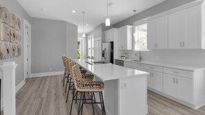 A modern kitchen with white cabinetry, a large island with bar stools, and a view of the outdoors through a window. - Steps From the Seagrove Beach - Gulf Views - Sleeps 10 - Community Pool (Santa Rosa Beach)