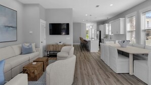 A modern, open-plan living and dining area with a neutral color palette, a flat-screen TV mounted on the wall, and a kitchen with white cabinetry. - Steps From the Seagrove Beach - Gulf Views - Sleeps 10 - Community Pool (Santa Rosa Beach)
