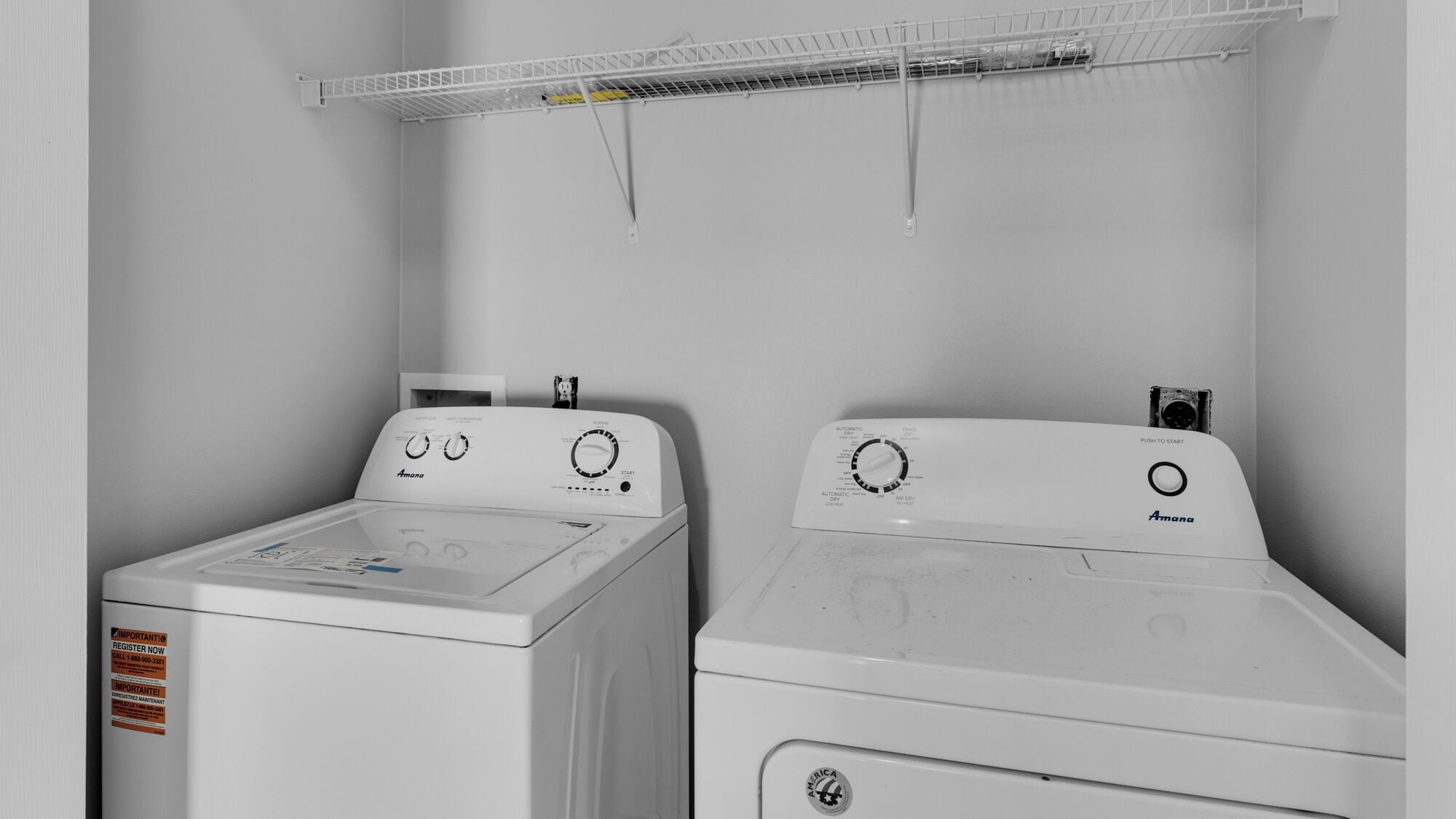A laundry room with two white Amana washing machines and a metal drying rack.