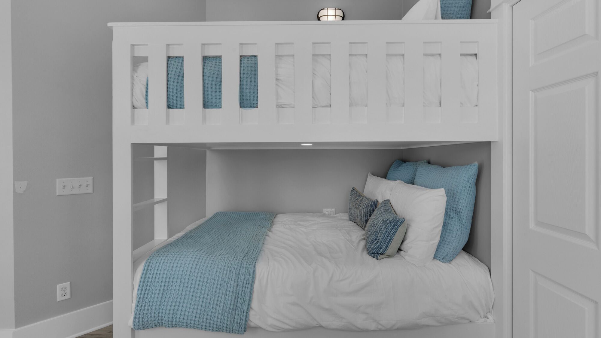 A bunk bed with a white frame, a blue and white bedspread, and several pillows.