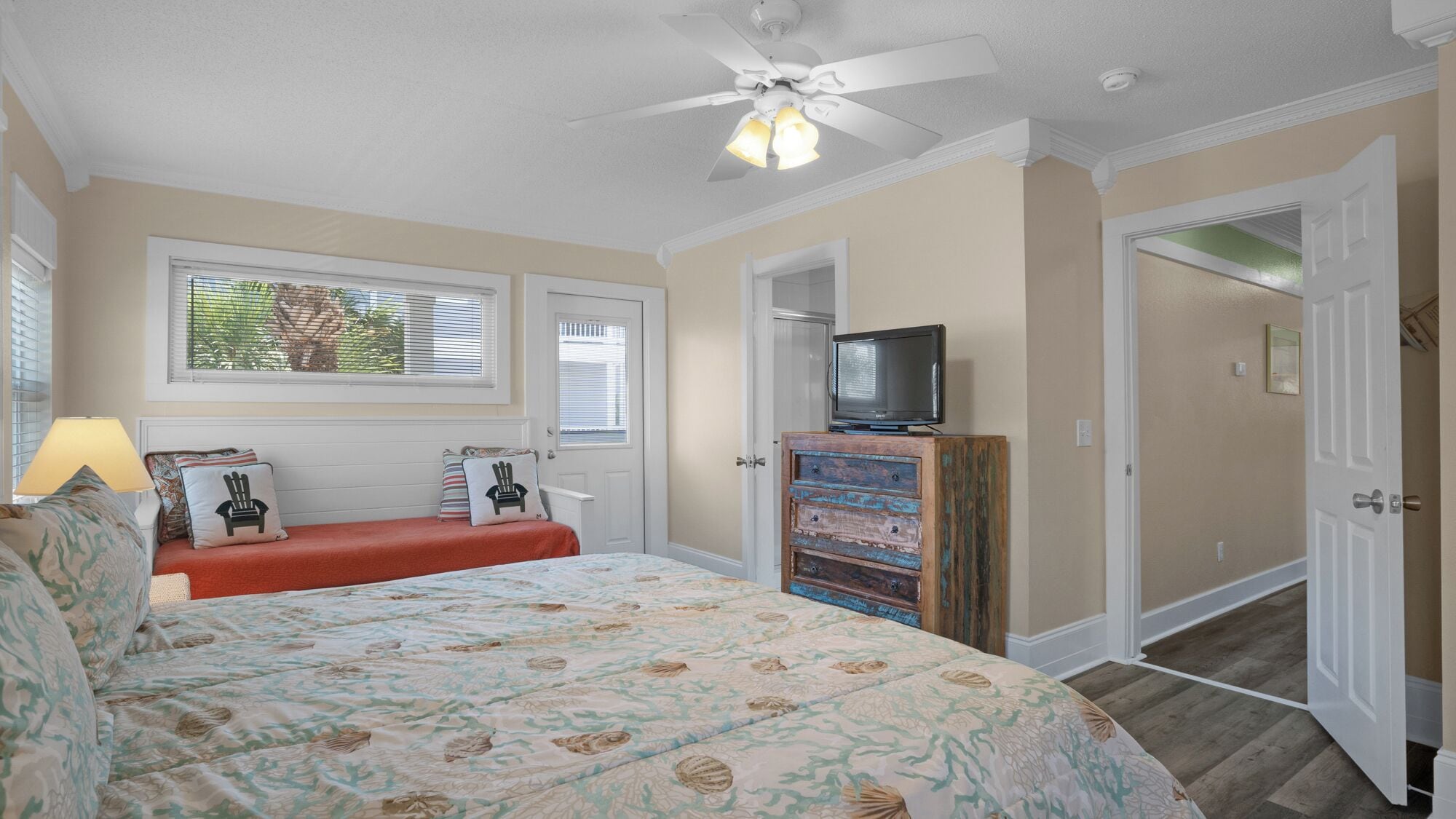 A bedroom with a bed, a television on a wooden cabinet, and a ceiling fan.