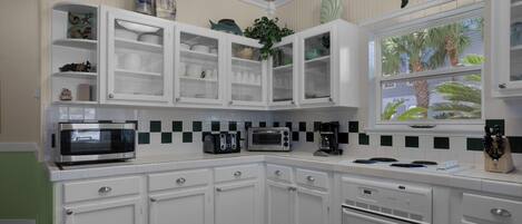 A kitchen with white cabinets, a microwave, a toaster, and a window with a view of palm trees.