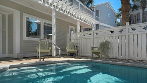 Una piscina con bordo in legno, due poltrone Adirondack e un recinto bianco decorato con sagome di animali.