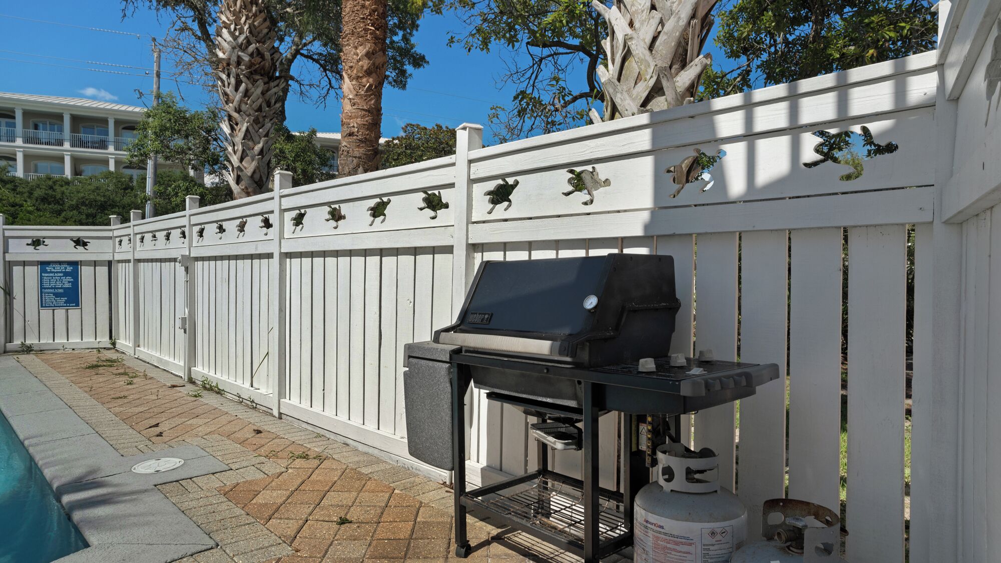 A barbecue grill with a gas tank and a metal rack, set against a white fence with decorative animal cutouts.