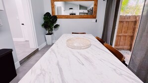 A modern dining area with a marble table, a large mirror, and a potted plant.