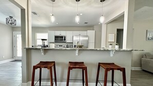 A modern kitchen with white cabinets, a marble countertop, and three wooden stools.