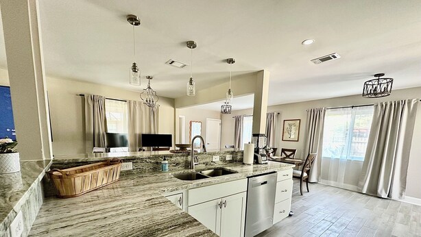 A modern kitchen with granite countertops, a dishwasher, and a dining area with a table and chairs.