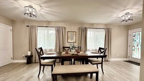 A dining room with a wooden table, four chairs, a bench, and two pendant lights.