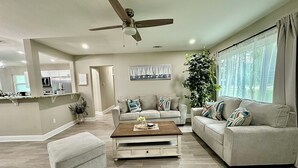 A modern living room with a ceiling fan, a large window with curtains, a sofa set, and a coffee table.
