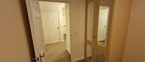 Une pièce avec un tapis beige, une armoire en bois et une porte blanche donnant sur une autre pièce.