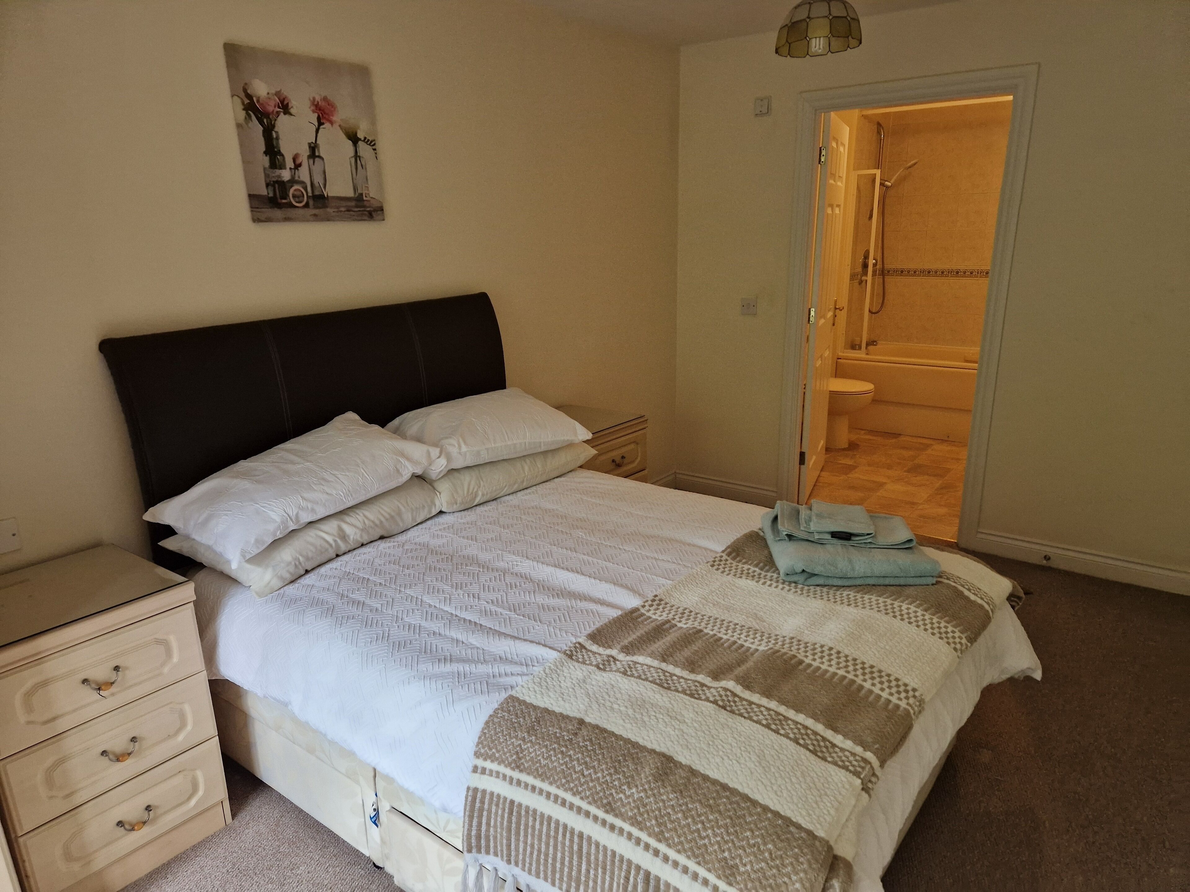 A neatly made bed with white linens and a brown and white striped blanket, a bedside table with a lamp, and a painting on the wall.