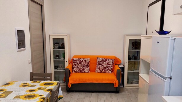 Un espace de vie compact comprenant un canapé, une table recouverte d’une nappe à motifs de tournesols et un réfrigérateur.
