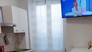 Une cuisine moderne avec des meubles blancs, une cuisinière à gaz et un coin repas doté d’une table recouverte d’une nappe à motifs de tournesols.