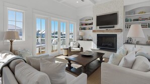A spacious living room with a fireplace, a television, and a bookshelf. - Stunning Luxury Beach Home: Gulf Views, Large Private Pool, Free Beach Setup! (Panama City Beach)