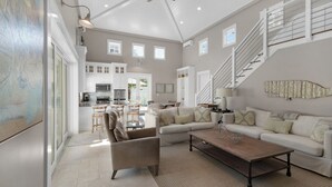 A spacious living area with a large sofa, a coffee table, and a dining area with chairs. There is a staircase leading to an upper level. - Stunning Luxury Beach Home: Gulf Views, Large Private Pool, Free Beach Setup! (Panama City Beach)
