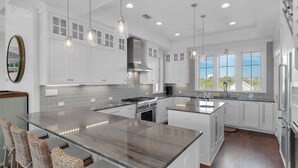 A modern kitchen with white cabinetry, a large island, and pendant lighting. - Stunning Luxury Beach Home: Gulf Views, Large Private Pool, Free Beach Setup! (Panama City Beach)