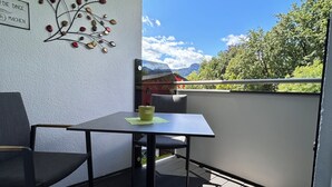 A balcony with a table and chairs, a decorative wall piece, and a view of greenery and mountains. - Ferienwohnung Silvia , Mondsee Zentrum (Mondsee)