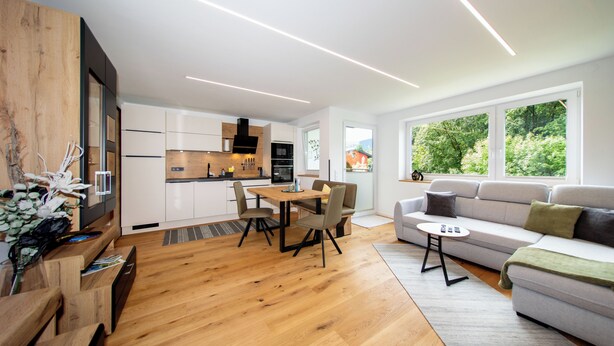 A modern living space with a wooden floor, a dining area with a table and chairs, a sofa, and a kitchen in the background. - Ferienwohnung Silvia , Mondsee Zentrum (Mondsee)