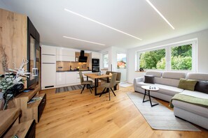 Un espacio habitable moderno con piso de madera, un área de comedor con mesa y sillas, un sofá y una cocina al fondo.