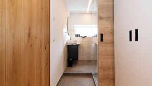 A hallway with wooden flooring, a black doormat, and a view into a bathroom with a mirror, sink, and cabinets. - Ferienwohnung Silvia , Mondsee Zentrum (Mondsee)