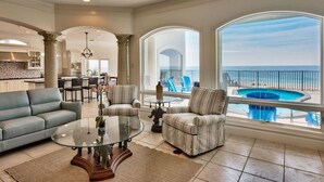 A spacious living area with a glass coffee table, a sofa, and armchairs, overlooking a pool and the ocean. - Stunning Views! 9BR Gulf Front Home, Pool, Elevator, Pool Table (Destin)