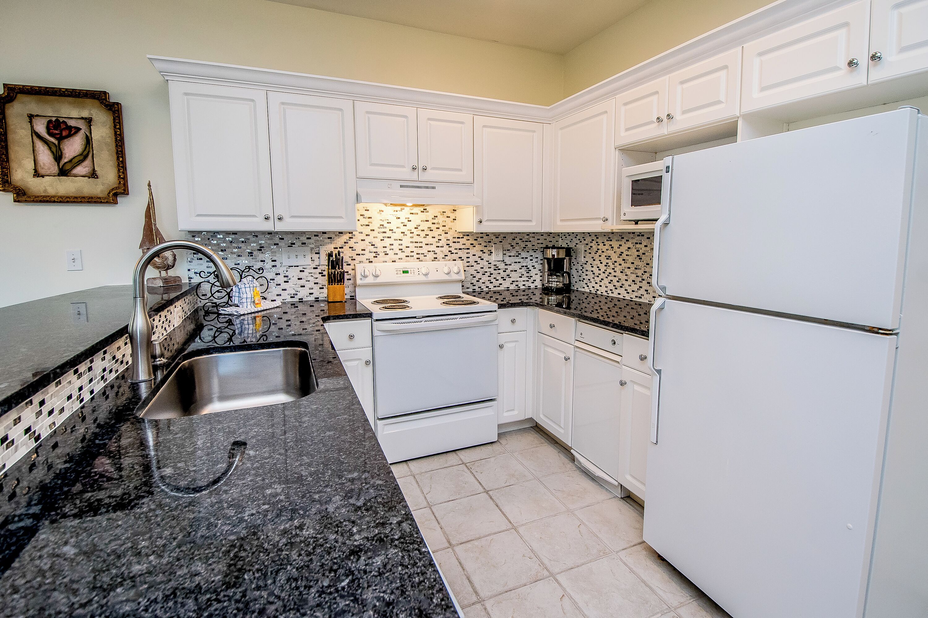 A kitchen with white cabinets, a granite countertop, a stainless steel sink, a white stove, and a white refrigerator.