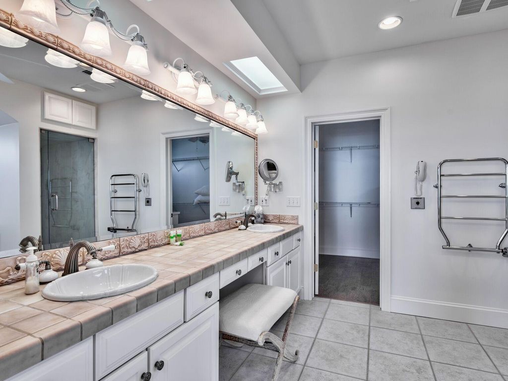 A modern bathroom with a large vanity, a double sink, a mirror with lights, a towel rack, and a shower area.