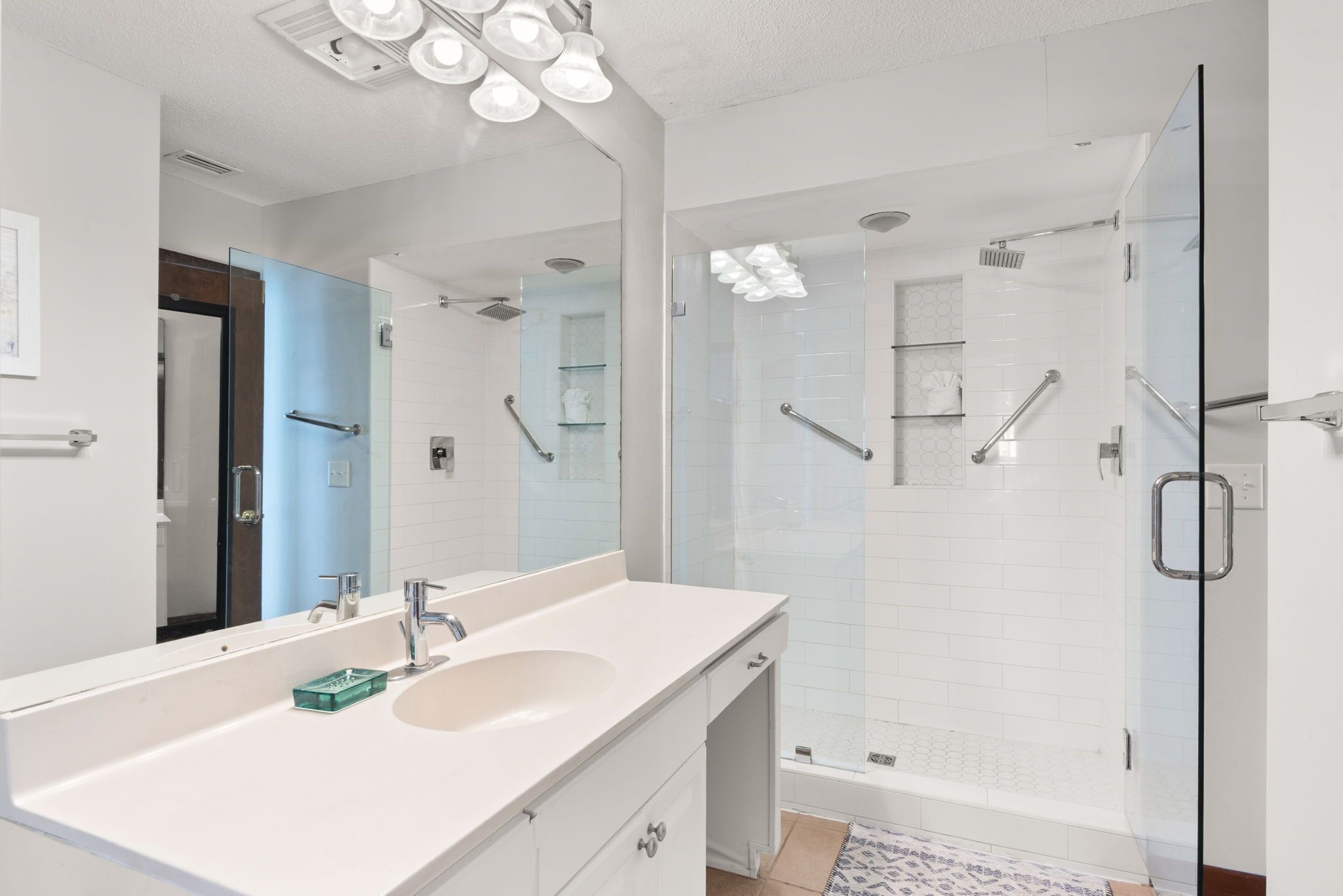 A modern bathroom with a large mirror, a white sink, and a glass-enclosed shower area.