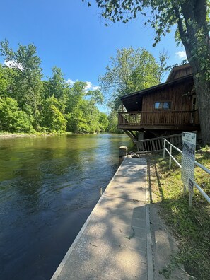 Una baita di legno con veranda affacciata su un fiume, immersa nel verde.