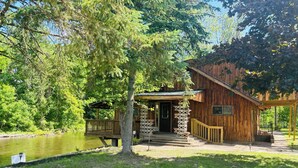 A rustic cabin with a wooden exterior, a porch, and a small deck overlooking a pond. - 6 Bed River Home, Right On St. Joseph River. (Union City)