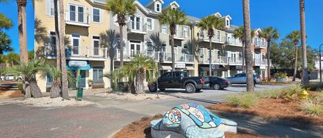 A multi-story residential building with balconies, palm trees, and a paved street.