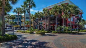 A multi-story hotel with a red facade, a balcony, and palm trees in the foreground. - The Salty Dog on 30a: Modern Updates, 1 Minute to the Beach! (Santa Rosa Beach)
